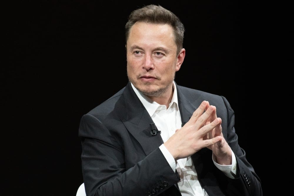 Elon Musk Met handen tegen elkaar in een pak zittend op een stoel