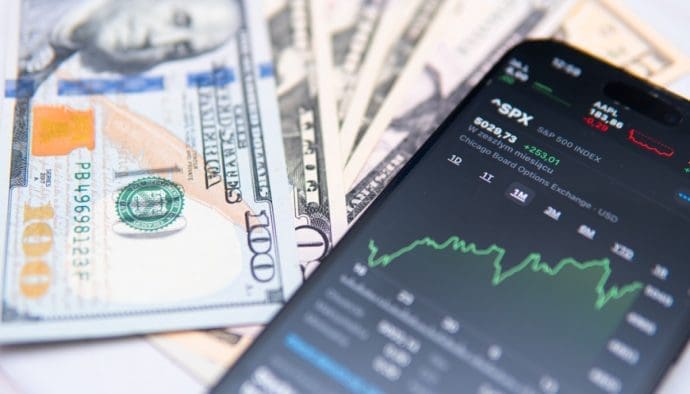 Afbeelding van mobiel op dollarbiljetten en de SP500 index