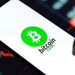 Een afbeelding van een telefoon met daarop het bitcoin cash (BCH) logo, met op de achtergrond een grafiek en marktdata