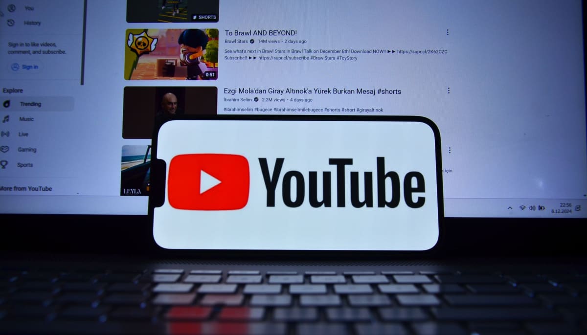 Het logo van Youtube op een mobiele telefoon met op de achtergrond een laptop met het YouTube interface en verschillende video's