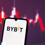 Het logo van cryptobeurs Bybit op een mobiele telefoon, met op de achtergrond een rode koers, representatief voor de koers van de gestolen ethereum (ETH)